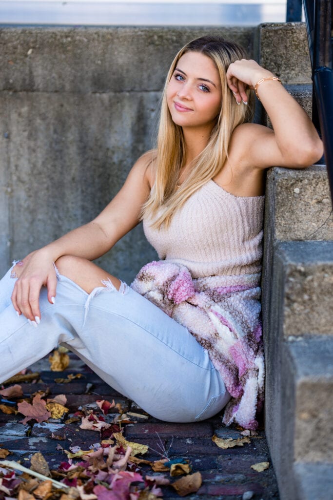 Senior girl sits outside 2nd Street Market in Dayton, Ohio during her senior pictures. She is wearing ripped jeans and a cute crop top.