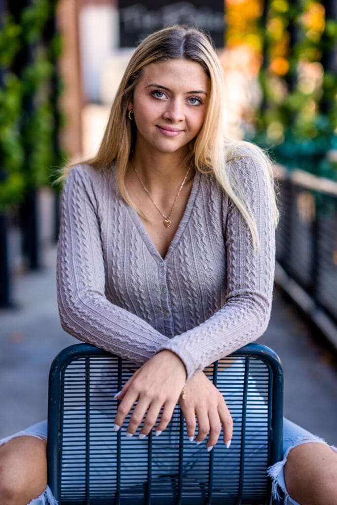 Senior girl sits in a metal chair in a walkway in downtown Dayton during her senior photos.