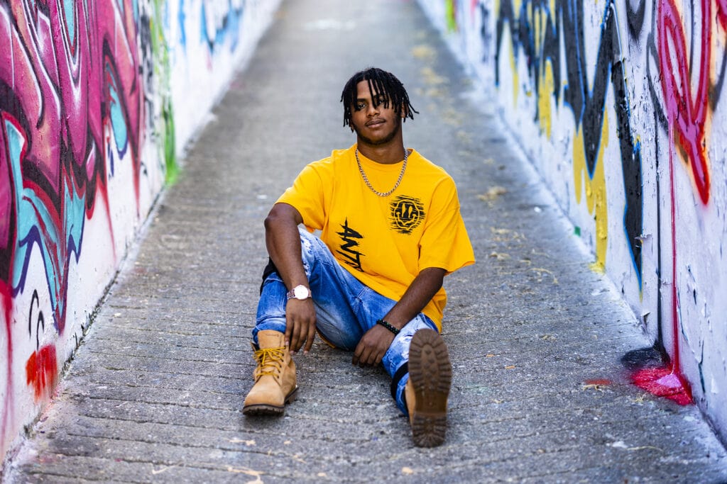 Senior guy sits in a graffiti alleyway in Dayton, Ohio during his senior portraits with Studio 22 Photography.